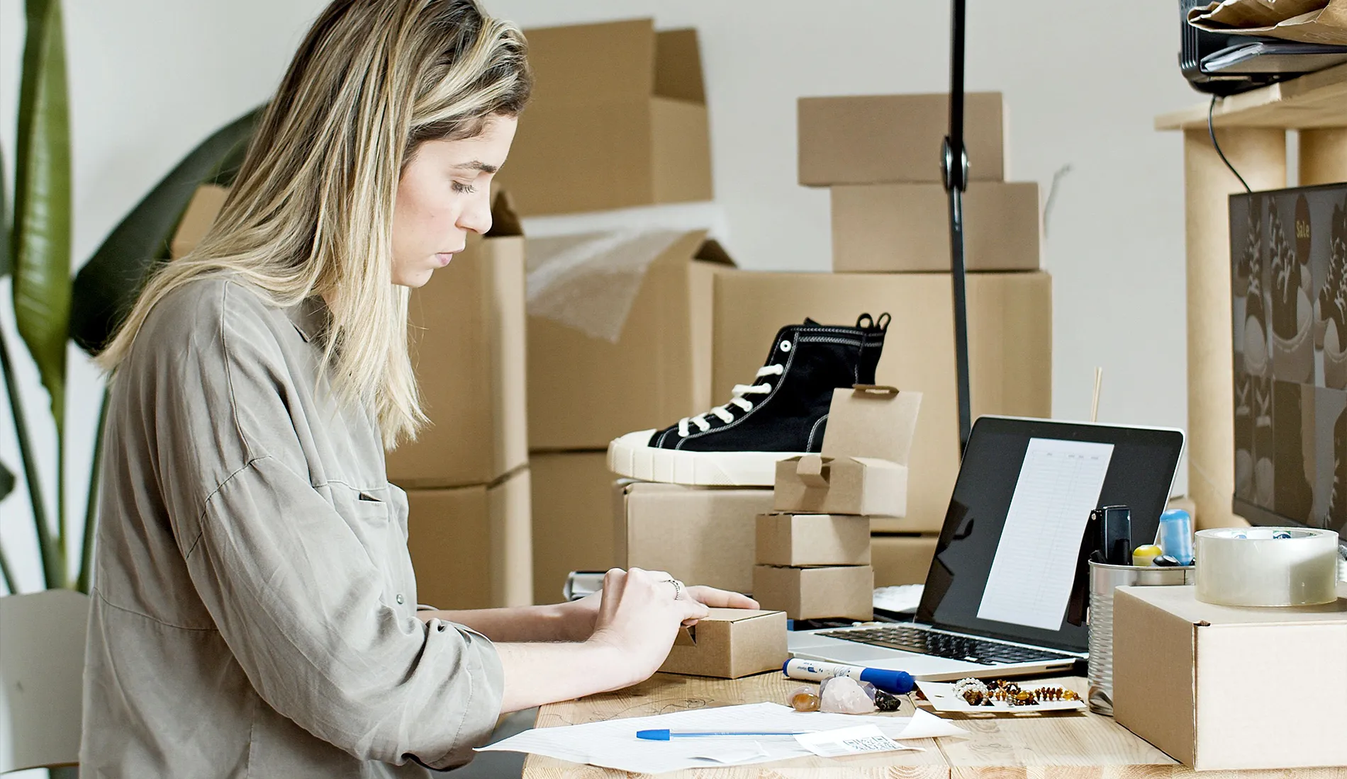 A woman packing boxes for her online store, surrounded by packaging materials and a laptop