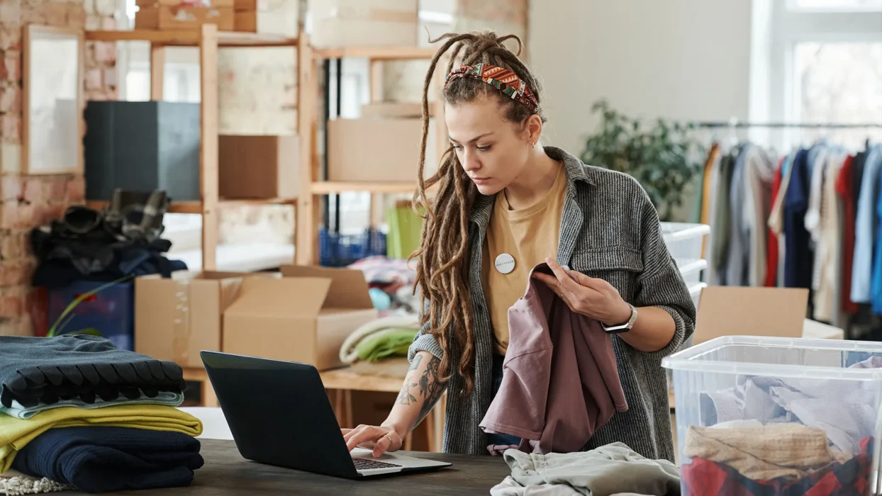 Woman with dreadlocks using a laptop while sorting clothes in a loft for volunteer work